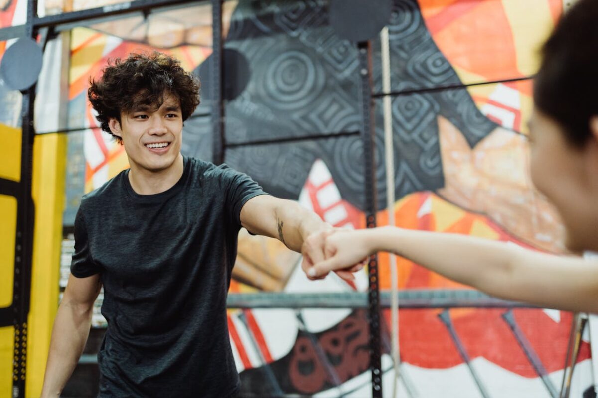 Two young adults in a colorful gym environment happily exchange a fist bump, symbolizing camaraderie and motivation.